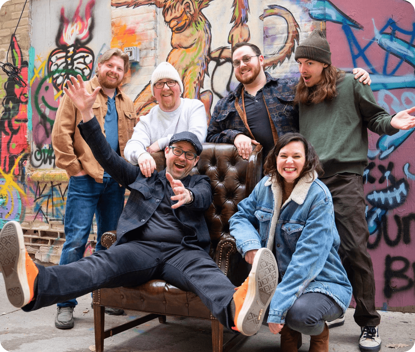Group of people posing in front of a graffiti-covered wall.