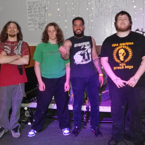 Four individuals standing together in a room with musical equipment and posters on the wall.