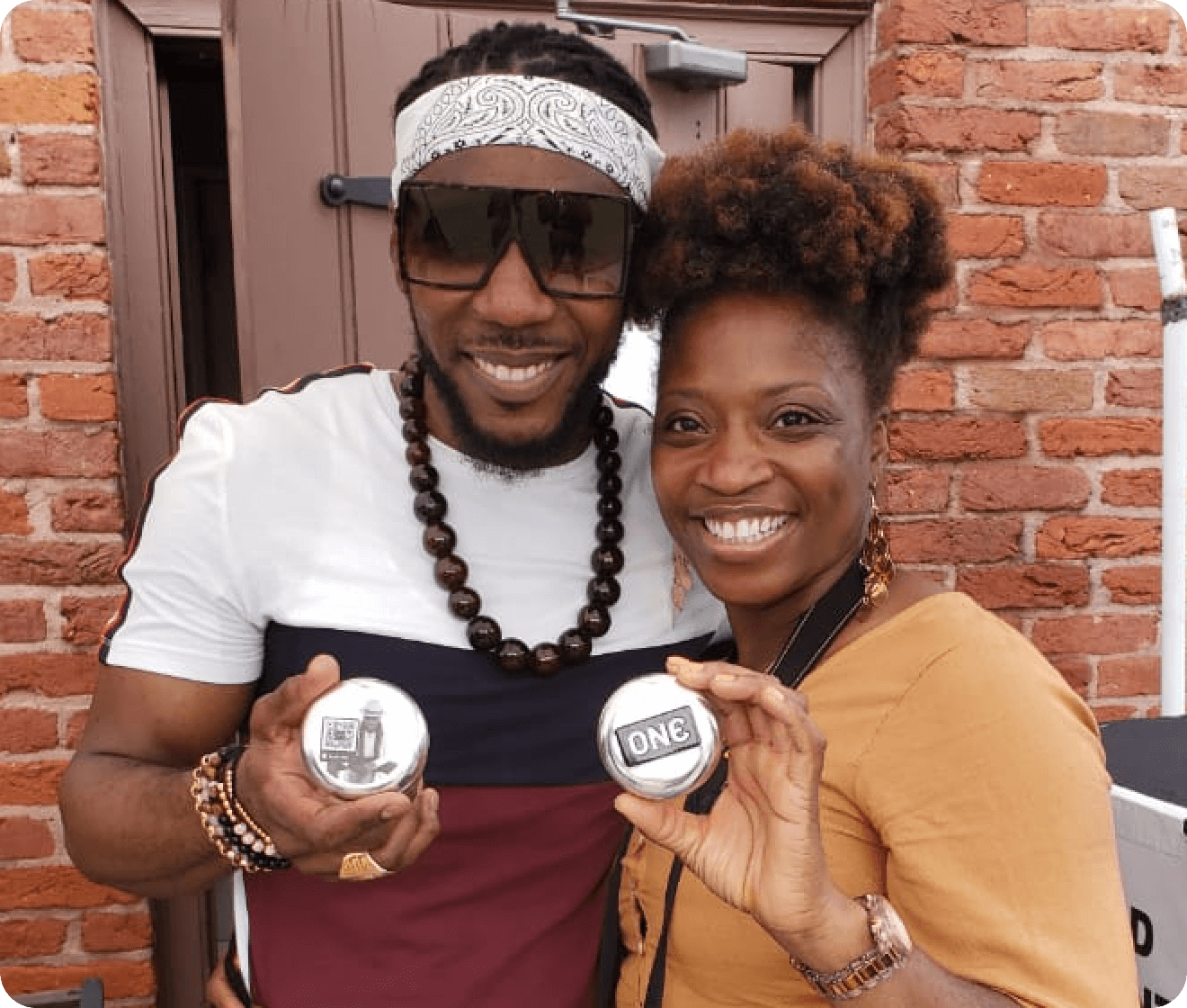 Two people holding 'ONE' branded items in front of a brick wall.